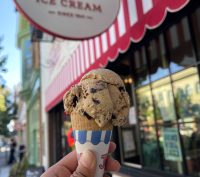 A hand holds up an ice cream cone in front of the Tucker's Ice Cream shop.