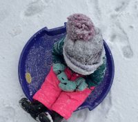 A child sitting on a round sled with gloves at Calaveras Big Trees State Park in winter